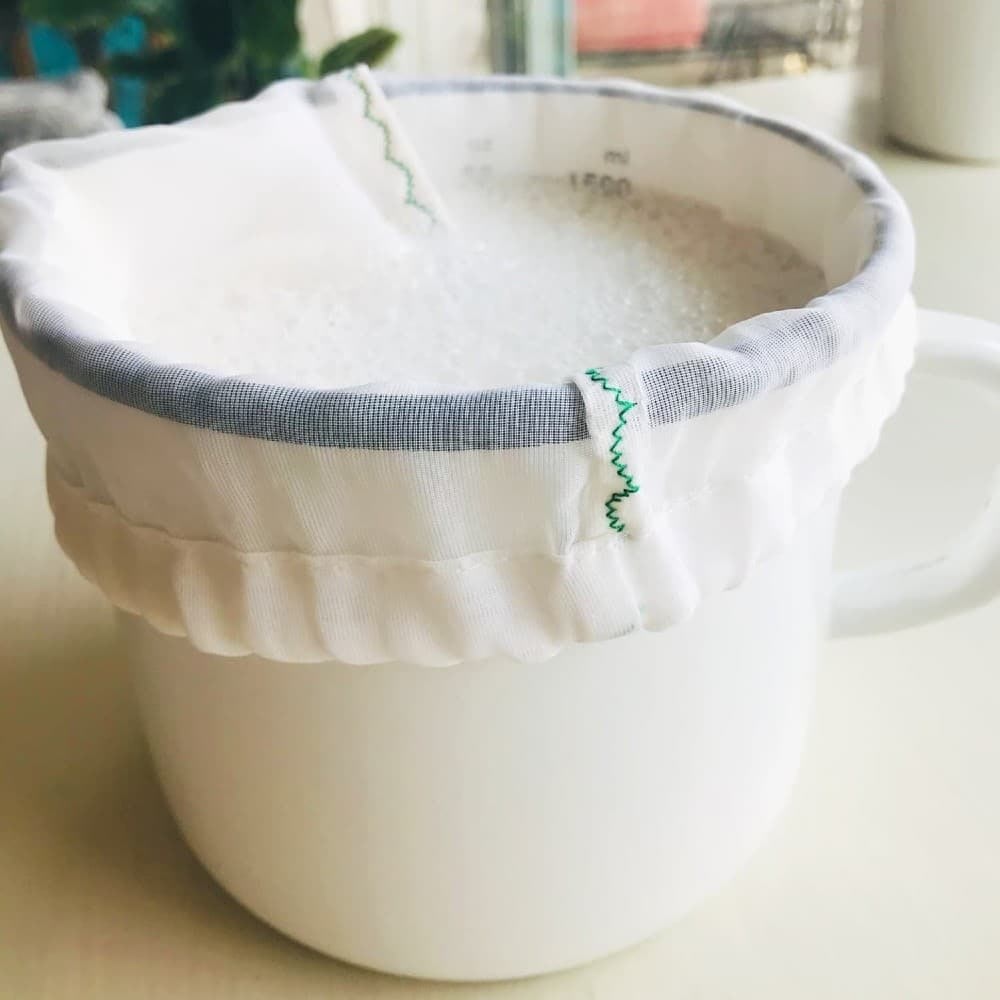 nut milk recipe, white ceramic pot lined with a white mesh bag, filled with white milk