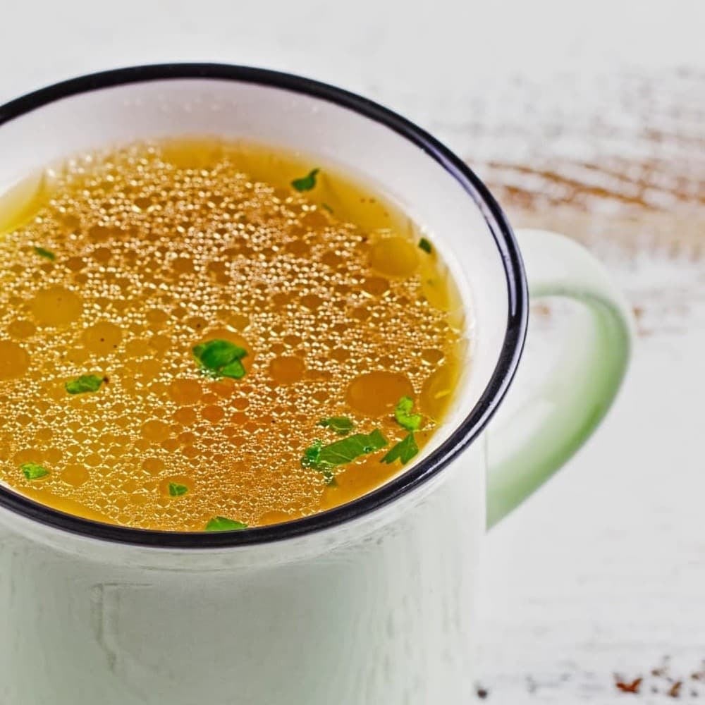 healing bone broth recipe, white ceramic mug filled with golden liquid broth